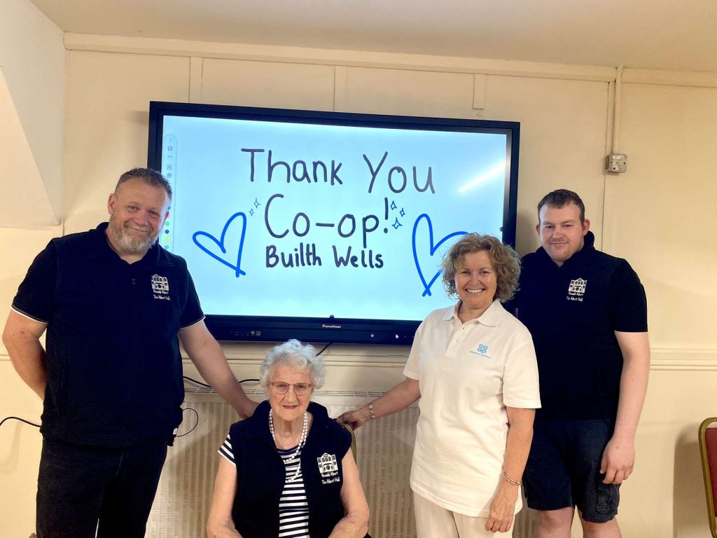 A group of 4 people in front of an interactive screening with the message 'Thank You Co-Op Builth Wells'